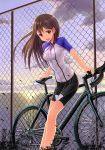  1girl bicycle bike_jersey bike_shorts brown_hair chain-link_fence clouds cloudy_sky highres leaf looking_at_viewer ocean original red_eyes sky smile solo sunset tsumiwara 