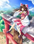 1girl :o blue_sky blush bow brown_hair clouds detached_sleeves frilled_skirt frills hair_bow hair_tubes hakurei_reimu highres leg_lift lens_flare long_hair looking_to_the_side mary_janes midriff mountain navel outdoors red_eyes shoes sitting_on_torii skirt skirt_set sky solo torii touhou unory wind 