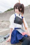  1girl arm_at_side black_legwear blue_skirt brown_eyes brown_hair closed_mouth cosplay day japanese_clothes kaga_(kantai_collection) kantai_collection kimono lips looking_at_viewer muneate outdoors photo serious short_hair short_sleeves side_ponytail sitting skirt solo 