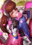  1girl bangs bodysuit breasts brick_wall brown_eyes brown_hair bubble_blowing bubblegum bunny_print cherry_blossoms d.va_(overwatch) day facepaint facial_mark foreshortening gloves gum hand_on_hip headphones highres holding holding_weapon long_hair looking_at_viewer magion02 medium_breasts nose one_eye_closed outdoors overwatch pilot_suit ribbed_bodysuit signature skin_tight smile solo standing weapon whisker_markings white_gloves 