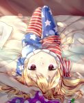  1girl :t american_flag_dress american_flag_legwear bed_sheet blonde_hair blush cheunes clownpiece dress hat highres jester_cap long_hair looking_at_viewer lying neck_ruff on_back on_bed pantyhose pillow polka_dot pout red_eyes short_dress short_sleeves solo star star_print striped touhou upside-down 