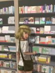  1girl bag blonde_hair blue_eyes blush book bookshelf casual facing_viewer fang girls_und_panzer hammer_and_sickle hettsuaa highres katyusha messenger_bag shirt shop shorts shoulder_bag solo t-shirt white_shirt 