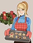  1girl apron baking_sheet blonde_hair breasts candle christmas_wreath cookie food highres large_breasts metroid oven_mitts ponytail samus_aran skin_tight smile splashbrush zero_suit 