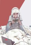  1girl absurdres altera_(fate) alternate_costume blanket candy candy_wrapper commentary_request computer dark_skin fate/extella fate/extra fate_(series) food grey_shirt headphones headphones_around_neck highres holding laptop long_hair pillow playing_games red_eyes reroi shirt sitting solo sweat two-tone_background under_covers veil white_hair 