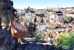  1girl apron black_hair black_shoes blue_sky check_commentary commentary commentary_request day dress highres kaisen long_hair looking_to_the_side orange_dress original outdoors plant portugal profile real_world_location scenery shadow shoes signature sky solo standing tree village wall 