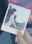  1girl 456 black_hair bridge city clouds commentary highres holding_photo long_hair looking_afar mole original photo_(object) polaroid pov pov_hands profile railing sky sunset water 