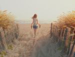  1girl artist_name barefoot beach brown_hair commentary day denim denim_shorts fence footprints from_behind holding long_hair original outdoors plant revision sandals shirt shorts signature silhouette solo striped striped_shirt tamaki_(tamaki_illust) walking water wind wooden_fence 