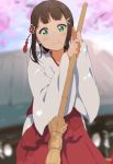  1girl bamboo_broom bangs black_hair blurry blurry_background blush broom flower green_eyes hair_flower hair_ornament hakama highres holding holding_broom icehotmilktea japanese_clothes kanzashi kurosawa_dia long_hair looking_at_viewer love_live! love_live!_school_idol_festival love_live!_sunshine!! miko mole mole_under_mouth smile solo wide_sleeves 