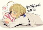  1girl ahoge amanekuu anger_vein artoria_pendragon_(all) bangs blonde_hair blush braid commentary_request eyebrows_visible_through_hair fate/stay_night fate_(series) frown hair_bun hair_ribbon heart highres long_sleeves lying on_bed on_stomach pillow pillow_hug pink_background pout ribbon saber shirt simple_background solo speech_bubble spoken_anger_vein tears translation_request under_covers white_shirt yes-no_pillow 