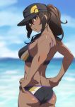  1girl ass bare_shoulders baseball_cap bikini black_bikini blue_sky blush breasts brown_eyes brown_hair commentary_request dark_skin day female_protagonist_(pokemon_go) from_behind fukushi_ryouhei hair_between_eyes hands_on_hips hat lips long_hair looking_at_viewer looking_back medium_breasts ocean outdoors pokemon pokemon_go ponytail shiny shiny_hair shiny_skin sky solo standing swimsuit 