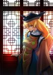  1girl bangs black_hat blonde_hair breasts brown_eyes commentary_request futoumeido green_skirt hat indoors large_breasts light_particles long_hair long_sleeves looking_at_viewer matara_okina profile skirt solo standing tabard touhou wide_sleeves window 