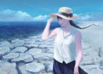  1girl bare_arms bare_shoulders beach black_bow black_hair blue_skirt blue_sky bow braid brown_eyes clouds floating_hair grass hand_up hat hat_bow highres long_hair ocean original outdoors parted_lips rock shirt single_braid skirt sky smile solo standing straw_hat tunapon01 white_shirt 