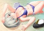  1girl arm_up barefoot beach bikini bird blue_bikini blue_eyes bow_bikini breasts cleavage closed_mouth day failure_penguin folded_leg hamakaze_(kantai_collection) highres kantai_collection leg_up looking_at_viewer lossy-lossless lying medium_breasts miss_cloud navel on_back outdoors partially_submerged penguin short_hair silver_hair smile solo sparkle swimsuit takehana_note wet 