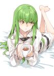  1girl barefoot c.c. code_geass creayus cup green_hair hood hoodie long_hair lying on_stomach parted_lips solo yellow_eyes 