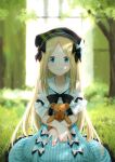  1girl abigail_williams_(fate/grand_order) alternate_costume bangs beret black_bow black_hat blonde_hair blue_eyes blurry blurry_background blush bow dress eyebrows_visible_through_hair fate/grand_order fate_(series) frilled_dress frills grass hair_bow hat holding holding_stuffed_animal kazuma_muramasa long_hair looking_at_viewer nature outdoors parted_bangs sitting sleeveless sleeveless_dress smile solo striped stuffed_animal stuffed_toy sunlight teddy_bear tree vertical-striped_dress vertical_stripes very_long_hair white_bow 