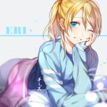  1girl artist_name ayase_eli bangs bed_sheet blonde_hair blue_eyes blue_shirt character_name chi_zu_crazy chin_rest eyebrows_visible_through_hair grey_pants grin hair_between_eyes long_hair looking_at_viewer love_live! love_live!_school_idol_project lying on_stomach one_eye_closed pants ponytail shirt smile solo swept_bangs under_covers 
