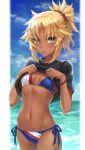  1girl :p bangs bikini black_shirt blonde_hair blue_bikini blue_sky blush braid breasts clouds commentary cowboy_shot english_commentary eyebrows_visible_through_hair fate/grand_order fate_(series) french_braid highres looking_at_viewer mordred_(fate)_(all) mordred_(swimsuit_rider)_(fate) navel ocean outdoors parted_bangs ponytail shirt shirt_lift short_hair short_sleeves side-tie_bikini sky small_breasts solo standing swimsuit tonee tongue tongue_out wet 