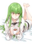  1girl bangs barefoot c.c. code_geass creayus cup eyebrows_visible_through_hair green_hair holding holding_cup hood hoodie legs_up long_hair looking_away lying on_stomach parted_lips solo straitjacket yellow_eyes 