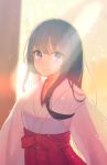  1girl backlighting bangs black_hair blurry blurry_background blush bow closed_mouth commentary_request eyebrows_visible_through_hair hakama highres hyakunin_momoko japanese_clothes kimono lens_flare long_hair looking_at_viewer miko mole mole_under_eye original red_bow red_hakama smile solo sunlight tareme upper_body violet_eyes white_kimono 