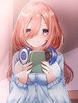  1girl bangs blue_cardigan blush book brown_hair closed_mouth commentary_request go-toubun_no_hanayome hair_between_eyes headphones headphones_around_neck highres holding holding_book long_hair looking_at_viewer makoto-0726 nakano_miku smile upper_body violet_eyes 
