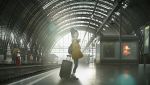  1girl backlighting backpack bag commentary hat jacket leggings lens_flare luggage mogumo original railroad_tracks scarf solo train_station train_station_platform waving 