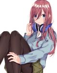  1girl absurdres bangs blue_cardigan blue_eyes blush brown_hair brown_legwear cardigan closed_mouth commentary_request eyebrows_visible_through_hair feet_out_of_frame go-toubun_no_hanayome green_skirt hair_between_eyes hand_on_headphones hand_up headphones headphones_around_neck highres knees_up long_hair long_sleeves looking_at_viewer nakano_miku norazura pantyhose pleated_skirt simple_background skirt sleeves_past_wrists solo white_background 