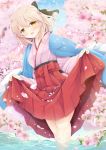  1girl ahoge bangs black_ribbon blonde_hair blue_sky blush cherry_blossoms commentary_request eyebrows_visible_through_hair falling_petals fate/grand_order fate_(series) hair_between_eyes hair_ribbon hakama half_updo iris_yayoi japanese_clothes kimono lifted_by_self looking_at_viewer okita_souji_(fate) okita_souji_(fate)_(all) outdoors ribbon short_hair sidelocks skirt skirt_lift sky smile solo standing wading water yellow_eyes 
