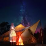  1girl blue_eyes campfire camping closed_mouth eyebrows eyebrows_visible_through_hair fire hair_ornament highres long_hair long_skirt looking_at_viewer milky_way night night_sky shima_rin skirt sky solo standing star star_(sky) tent violet_eyes yurucamp 
