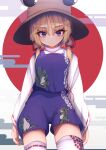  1girl animal_print bangs blonde_hair blue_eyes brown_headwear closed_mouth clouds cowboy_shot darumoon egasumi eyebrows_visible_through_hair frog_print highres long_sleeves looking_at_viewer medium_hair moriya_suwako outdoors purple_shorts purple_vest red_circle ribbon-trimmed_legwear ribbon-trimmed_sleeves ribbon_trim shirt shorts sidelocks solo standing thigh-highs touhou vest white_shirt wide_sleeves 