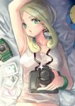  1girl armpits bare_shoulders bed_sheet blonde_hair blush breasts camera collarbone commentary_request e-co eyelashes from_above gen_3_pokemon glint green_eyes green_wristband holding holding_camera looking_at_viewer lying navel on_back open_mouth photo_(object) pokemon pokemon_(game) pokemon_xy shiny shiny_hair solo surskit tank_top upper_body viola_(pokemon) white_tank_top 