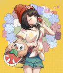  1girl bangs beanie black_hair character_name closed_mouth eyebrows_visible_through_hair floral_print gen_7_pokemon green_shorts hat heart highres holding holding_poke_ball holding_strap kazuru_wa one_eye_closed poke_ball poke_ball_(basic) pokemon pokemon_(creature) pokemon_(game) pokemon_sm red_headwear rowlet selene_(pokemon) shirt short_shorts short_sleeves shorts smile symbol_commentary t-shirt tied_shirt 