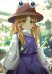  1girl animal_print bangs blonde_hair bloom blurry blurry_background blush brown_headwear closed_mouth commentary_request cowboy_shot frog_print hat highres long_hair long_sleeves moriya_suwako multicolored multicolored_background murasaki_tsutsuji parted_bangs purple_sash purple_skirt purple_vest sash shirt sidelocks skirt skirt_set sleeves_past_wrists standing touhou turtleneck v-shaped_eyebrows vest white_shirt wide_sleeves yellow_eyes 