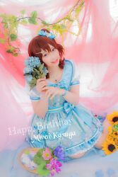  1girl blue_dress blue_flower brown_eyes brown_hair character_name commentary_request cosplay cosplay_photo dress flower hair_ornament hairclip happy_birthday highres holding holding_flower idolmaster idolmaster_million_live! idolmaster_million_live!_theater_days jewelry kasuga_mirai kasuga_mirai_(cosplay) looking_at_viewer necklace one_side_up photo_(medium) real_life short_sleeves sitting solo sunflower voice_actor voice_actor_connection yamazaki_haruka 