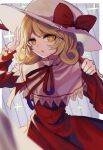  1girl blonde_hair blurry blurry_foreground border bright_pupils capelet commentary_request cowboy_shot curly_hair depth_of_field dress elly_(touhou) hand_up hat hat_ribbon highres holding holding_scythe ishikawa_sparerib juliet_sleeves long_sleeves looking_at_viewer medium_hair neck_ribbon outside_border parted_lips puffy_sleeves red_dress red_neckwear red_ribbon ribbon scythe solo standing touhou touhou_(pc-98) white_border white_headwear yellow_eyes 