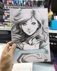  1girl 2017 art_tools_in_frame artist's_hand_in_frame blue_eyes blue_shirt cape closed_mouth collarbone commentary dc_comics english_commentary highres long_hair looking_at_viewer marker_(medium) partially_colored photo_(medium) shirt signature solo stanley_lau straight-on supergirl superman_(series) superman_logo traditional_media upper_body 
