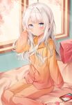 1girl :o ahoge arm_support bangs blue_eyes blush cellphone commentary_request day eyebrows_visible_through_hair hand_in_hair highres indoors long_hair long_sleeves looking_at_viewer on_bed orange_pajamas orange_pants original pajamas phone pillow sayu_(mini_2704) sitting sitting_on_bed smartphone solo white_hair window 