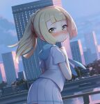  1girl bangs blonde_hair blunt_bangs blush building clenched_hand closed_mouth clouds commentary_request day fence floating_hair green_eyes hand_up lamppost leaning_forward lillie_(pokemon) long_hair looking_back outdoors pleated_skirt pokemon pokemon_(game) pokemon_sm ponytail shamonabe shiny shiny_hair shirt short_sleeves skirt sky solo water white_shirt white_skirt window 