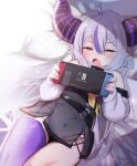  1girl absurdres bare_shoulders belt blush braid fang hair_between_eyes highres hololive horns la+_darknesss long_hair lying nintendo_switch on_back open_mouth pillow pointy_ears purple_hair purple_legwear silver_hair single_thighhigh solo thigh-highs utsusumi_kio very_long_hair virtual_youtuber yellow_eyes 