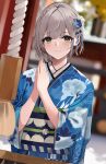  1girl bangs blue_flower blue_kimono blurry blurry_background blush closed_mouth commentary_request eyebrows_visible_through_hair floral_print flower green_eyes hair_flower hair_ornament hands_up highres hololive japanese_clothes kimono long_sleeves looking_at_viewer niii_(memstapak) obi own_hands_together print_kimono sash shirogane_noel short_hair silver_hair smile solo upper_body virtual_youtuber white_flower 