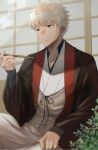  1boy bangs commentary_request emiya_shirou fate/grand_order fate_(series) highres holding igote japanese_clothes leaf long_sleeves male_focus mct open_mouth plant senji_muramasa_(fate) short_hair smile solo wooden_door yellow_eyes 
