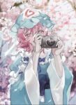  1girl :d blue_headwear blurry blurry_background camera cherry_blossoms covered_mouth depth_of_field hat highres holding holding_camera japanese_clothes long_sleeves mob_cap newbokk open_mouth outdoors petals pink_eyes pink_hair saigyouji_yuyuko short_hair smile solo touhou tree triangular_headpiece wide_sleeves 