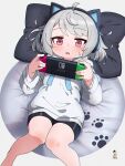 1girl ahoge animal_ears bean_bag_chair bike_shorts black_shorts cat_ear_headphones chromatic_aberration drawstring eyebrows_visible_through_hair fake_animal_ears feet_out_of_frame grey_background grey_hair handheld_game_console hands_up headphones highres holding hood hood_down hoodie knees_together_feet_apart kuro_kosyou long_sleeves lying nintendo_switch on_back original parted_lips paw_print paw_print_pattern pillow short_hair shorts simple_background solo sweatdrop violet_eyes 