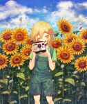  100momom 1boy bangs basil_(omori) birthday blonde_hair blush camera commentary_request daisy dated facing_viewer feet_out_of_frame flower green_shirt hair_flower hair_ornament happy_birthday highres holding holding_camera male_focus omori open_mouth orange_flower overalls shirt short_hair smile solo sunflower white_flower yellow_flower 