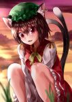  1girl absurdres animal_ear_fluff animal_ears arms_between_legs blurry blurry_foreground brown_hair cat_ears cat_tail chen clouds cloudy_sky commentary_request depth_of_field earrings eyebrows_visible_through_hair fang feet_out_of_frame frilled_skirt frills grass green_headwear hair_between_eyes hat highres jewelry long_sleeves looking_at_viewer maboroshi_mochi mob_cap multiple_tails open_mouth outdoors red_eyes red_skirt red_vest shirt short_hair single_earring skirt sky solo tail touhou twilight two_tails vest white_shirt 