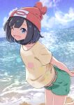  1girl ;d absurdres arms_behind_back beach beanie black_hair blue_eyes blue_sky clouds day floral_print foot_up from_side green_shorts hat highres leaning_forward looking_at_viewer negimiso1989 ocean one_eye_closed open_mouth outdoors own_hands_together pokemon pokemon_(game) pokemon_sm red_headwear selene_(pokemon) shirt short_hair short_shorts shorts sky smile solo standing standing_on_one_leg t-shirt water yellow_belt yellow_shirt 