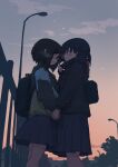  2girls backpack bag bangs black_hair black_jacket blush breath clouds evening eye_contact fence from_side hair_between_eyes highres holding_hands jacket lamppost long_sleeves looking_at_another multiple_girls natsuno_kanasemi original outdoors parted_lips pink_sky school_uniform skirt sky yuri 