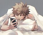  1boy bakugou_katsuki bare_arms bare_shoulders blanket blonde_hair boku_no_hero_academia commentary_request grey_background highres holding holding_phone lying male_focus on_stomach open_mouth phone pillow red_eyes sesami_dkt short_hair simple_background solo spiky_hair under_covers 