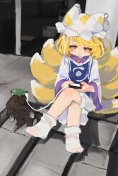  1girl absurdres animal_hat animalization blonde_hair blue_tabard brown_cat cat cellphone chen chen_(cat) commentary crossed_legs dress earphones fox_tail green_hat gumingdi_ban hat highres holding holding_phone kitsune mob_cap multiple_tails one_eye_closed phone shared_earphones sitting smartphone smile socks tabard tail touhou two_tails white_dress white_hat white_socks yakumo_ran yellow_eyes 