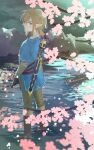  1boy blonde_hair blue_eyes blue_tunic boots branch brown_footwear cherry_blossoms closed_mouth commentary_request day fingerless_gloves from_behind gloves hair_between_eyes highres link looking_at_viewer looking_back male_focus master_sword outdoors pointy_ears rock solo sword the_legend_of_zelda the_legend_of_zelda:_breath_of_the_wild wading water weapon zmauuchan 