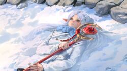  1girl absurdres blue_scarf coat commentary elf english_commentary frieren from_above green_eyes highres holding holding_staff light_blush lying mage_staff medium_hair on_back outdoors parted_bangs parted_lips pointy_ears qmori rock scarf snow solo sousou_no_frieren staff thick_eyebrows twintails twitter_username upper_body white_coat white_hair 